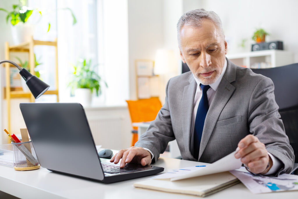Focused good-looking senior man with stubble checking documents